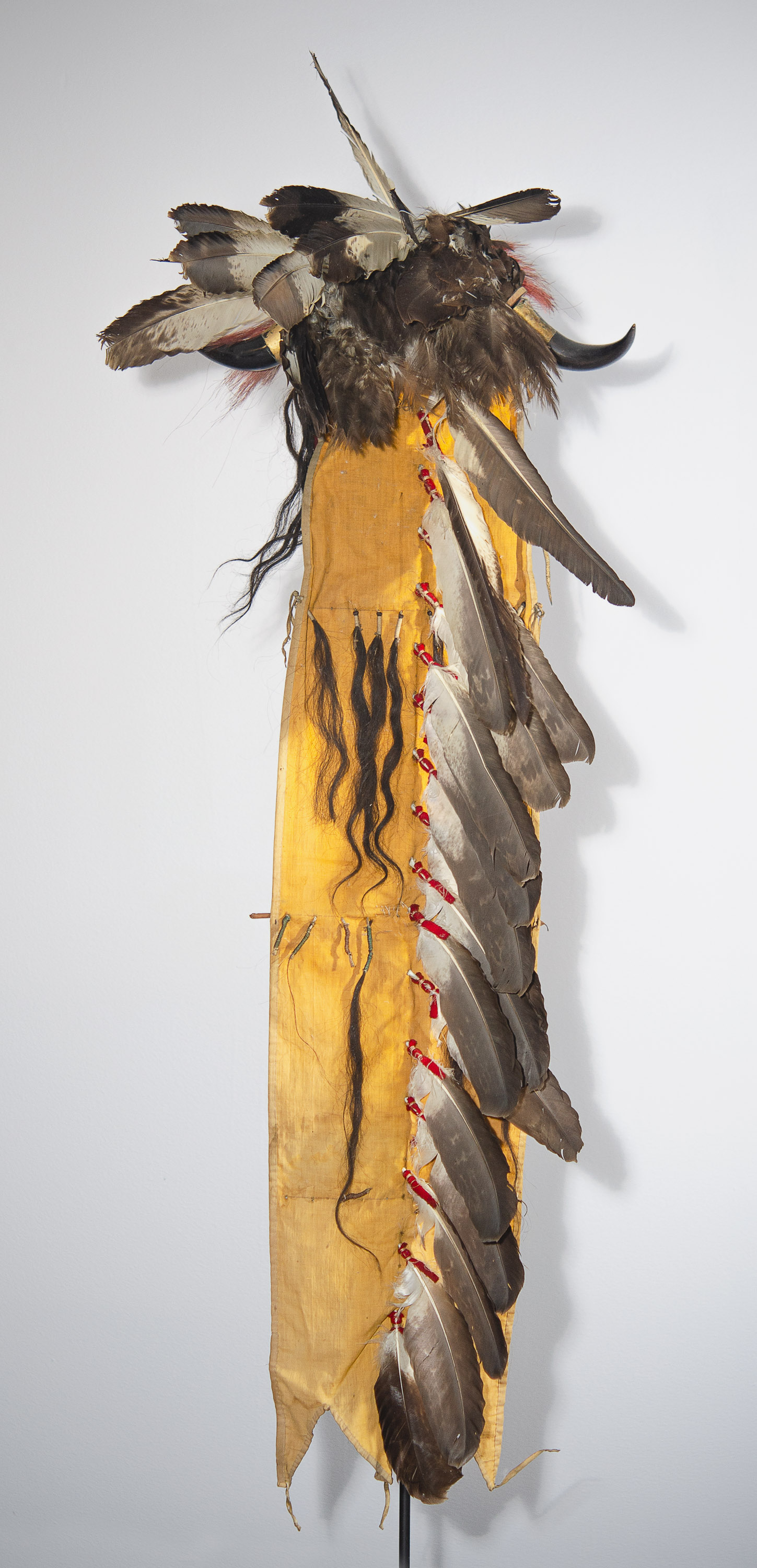 A yellow scarf-like piece of fabric decorated with swatches of animal hair, bird feathers, and bison horns.