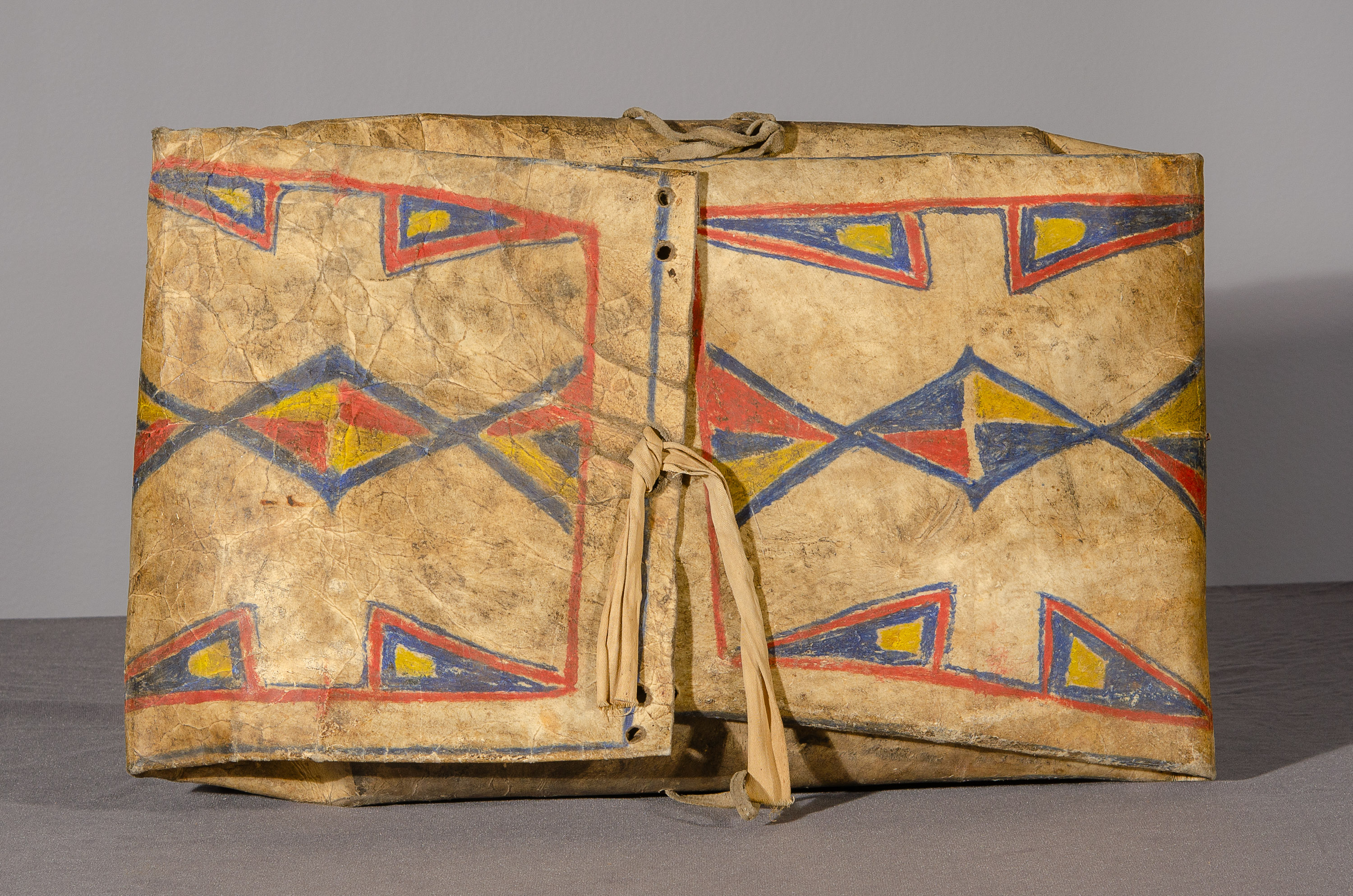 A folded animal hide knapsack decorated with blue, yellow, and red diamond designs.