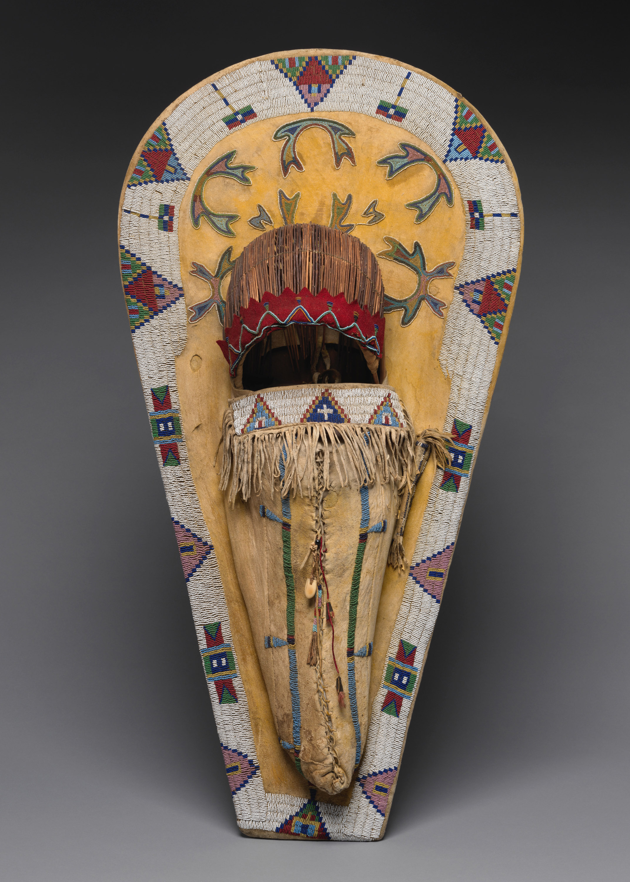 A Native American cradleboard with a beaded design around the edges and an animal hide pouch decorated with beaded designs and fringe.
