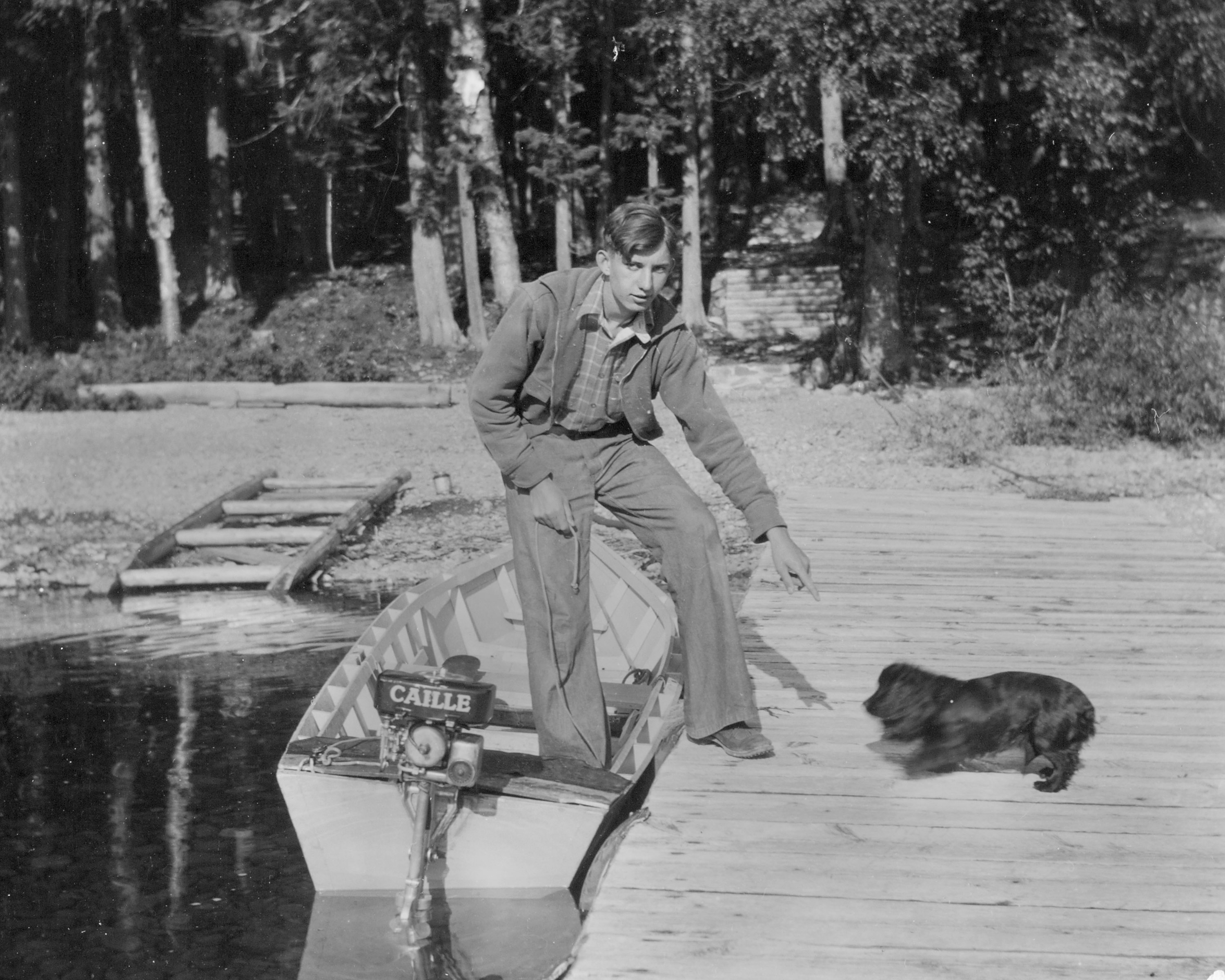 A black-and-white photograph of a young White man stepping from a small boat onto a dock where a small dog waits.